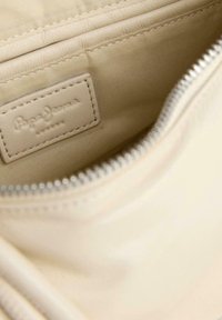 Borsa in tessuto beige con una superficie liscia, dotata di chiusura con zip e un sottile etichetta logata in rilievo all'interno.