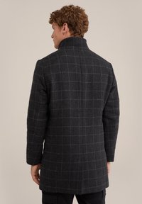 Svart rutigt kapp med hög krage, texturerad tyg, långa ärmar och rak skärning, med ett grått rutmönster mot en mörk bakgrund.