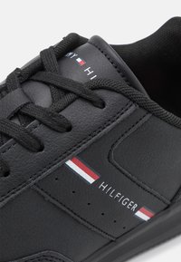 Baskets en cuir noir avec lacets, détails perforés et le nom de la marque "Hilfiger" avec des accents rouge, blanc et bleu.