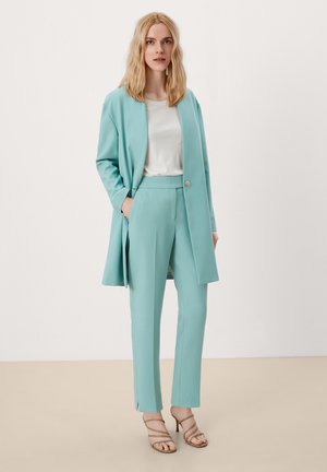Blazer ajusté bleu clair et pantalon assorti en tissu lisse, avec un top blanc en dessous, associé à des talons beiges à lanières.