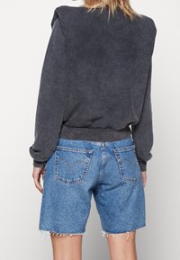 Szara bluza z przesadnie szerokimi ramionami, zestawiona z niebieskimi szortami dżinsowymi z postrzępionymi brzegami i tylnymi kieszeniami z charakterystycznym przeszyciem.