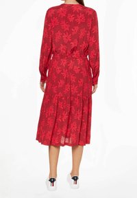 Abito midi rosso floreale con maniche lunghe, vita elastica, gonna a strati e tessuto trasparente; abbinato a sneakers bianche.