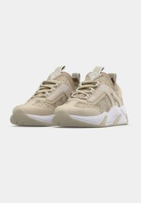 Baskets beiges avec une tige en tissu texturé, des accents blancs et des semelles en caoutchouc prononcées ; dotées de lacets et d'un logo sur la languette.