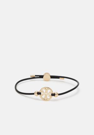 Pulsera de cuero negro con un charm circular dorado que presenta un diseño cortado intrincado y acentos metálicos cerca del cierre.