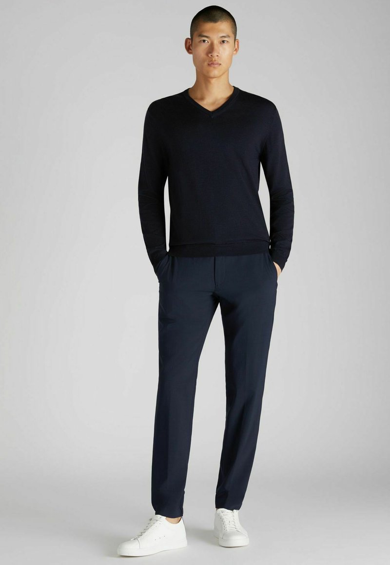 Marineblauer V-Ausschnitt-Pullover aus feinem Strick, kombiniert mit marineblauen, schmalen Hosen und weißen Sneakers. Einfaches, modernes Design mit weichem Material.