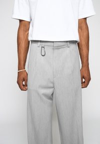 Pantalones grises ajustados con una textura suave, un corte holgado y un detalle metálico en el cinturón, combinados con una camiseta blanca básica.