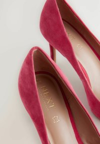 Scarpe scollate fucsia in suede con design a punta. Presentano un logo dorato sulla soletta interna, mostrando una finitura liscia e strutturata.