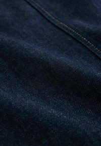 Donkerblauwe denimstof met een gestructureerd oppervlak en een zichtbaar weefpatroon. Heeft subtiele contrasterende stiksels. Ideaal voor kleding.