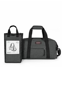 Gray fabric duffel bag with black accents, top handles, a front zipper pocket, and a smaller tote with a product label attached.