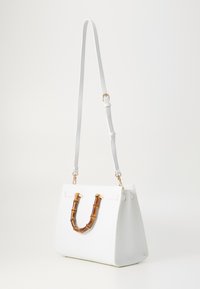 Witte leren handtas met een ronde vorm, gouden hardware en een bamboe accent handvat. Verstelbare schouderriem voor veelzijdigheid. Gladde textuur.