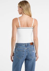 Biely priliehavý tielko s nastaviteľnými ramienkami a horizontálnym čiernym pruhom; skombinované s džínsovými nohavicami vysokého pásu v modrej farbe s logom.