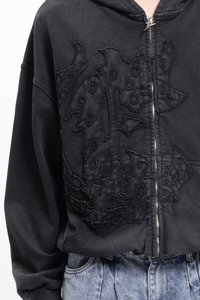 Haut à zip noir avec un design texturé brodé sur le devant. Comprend une capuche et des manches larges, associé à un bas en denim.