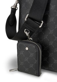 Musta teksturoitu nahkalaukku, jossa on irrotettava vetoketjullinen lompakko. Sisältää metalliset laitteet, hihnan kiinnitykset ja hienovaraisen kuvion pinnoilla.