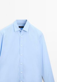 Lichtblauw langesleeve shirt van gladde stof. Heeft een puntige kraag, sluiting met knopen aan de voorkant en witte knopen langs de knoopsluiting.