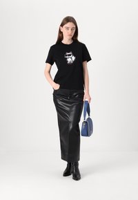 Černé tričko s bílým kresleným kočkovitým designem, doplněné černou koženou maxi sukni a modrou kabelkou. Model má na sobě černé kotníkové boty.
