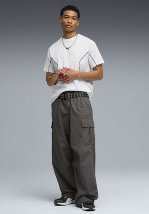 Weißes T-Shirt mit schwarzer Paspelierung, kombiniert mit locker sitzender grauer Cargo-Hose mit Seitentaschen und schwarzen Sneakers mit weißen Akzenten.