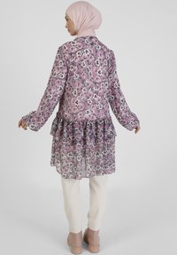 Long, purple floral chiffon blouse with a ruffled hem, paired with cream pants and light brown ankle boots. Long sleeves with button cuffs.