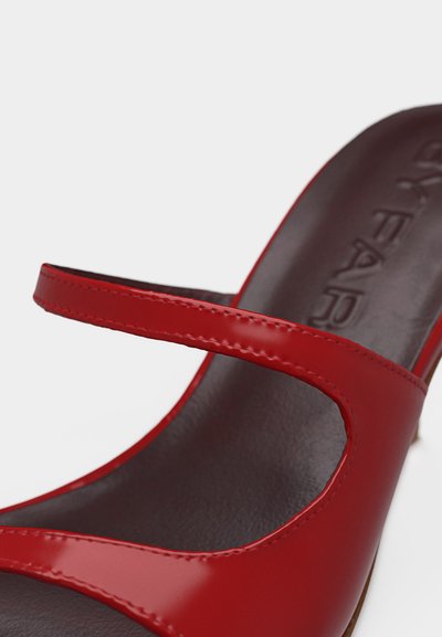 Červené lakované kožené otvorené mule s dvoma pásikmi a tmavou vložkou s ražbou názvu značky.