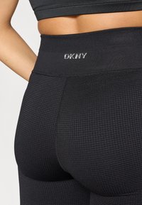 Μαύρα κολάν DKNY με υφασμάτινο μοτίβο, ψηλή ζώνη μέσης και λεπτομέρεια με λογότυπο. Το υλικό φαίνεται ελαστικό και εφαρμοστό για άνεση.