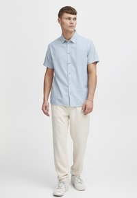 Lichtblauw overhemd met korte mouwen en kraag, voorzien van houten knopen. Gekozen in combinatie met crème kleurige broeken en witte sneakers.