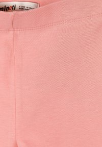 Lágy rózsaszín pamutszövet látható varrással és részben látható címkével, amely a márkanevet, a 3-4 éves méretet és a Bangladesben készült feliratot mutatja.