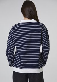 Maglietta a righe blu navy e bianca con maniche lunghe, colletto bianco e orlo a coste, realizzata in tessuto morbido, con una vestibilità rilassata e un design semplice.