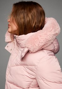 Puhasta jakna u mekoj ružičastoj boji s flufastim ružičastim krznenim kapuljačom, s patentnim zatvaračem i dugmadi, sa šivenim detaljima i quilted teksturom.