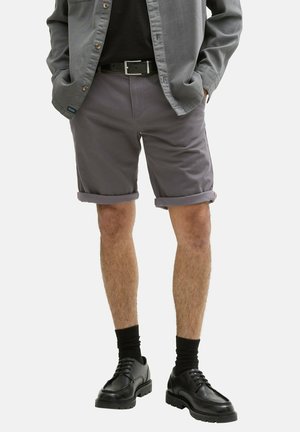 Pantaloni corti in tessuto grigio con risvolti, abbinati a una cintura nera e scarpe nere. L'outfit presenta un design moderno e casual.