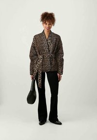 Casaco envolvente em padrão de leopardo com um cinto atado, apresentando um corte solto, mangas largas e uma textura suave. Combinado com calças flare pretas e uma bolsa.