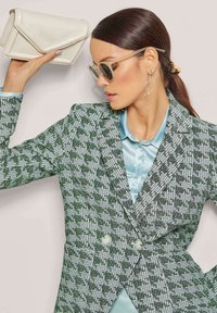 Grüner und weißer Hahnentritt-Blazer mit doppelreihigem Design, kombiniert mit einem hellblauen Satinkleid und einer weißen, strukturierten Clutch.