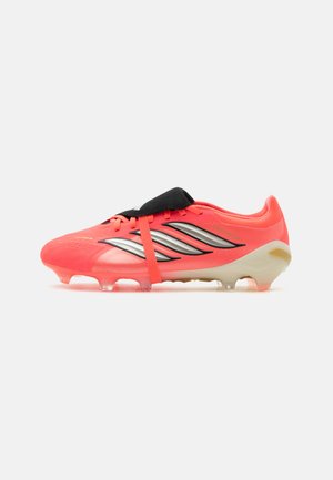 Botas de fútbol color coral brillante con rayas negras y plateadas, solapa para cubrir los cordones y tacos translúcidos en la suela.