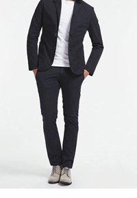 Czarna bawełniana marynarka na białej koszulce, zestawiona z czarnymi spodnimi w slim fit oraz jasnoszarymi butami na sznurowadła. Minimalistyczny design, bez wzorów.
