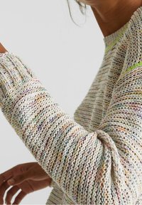 Stickad tröja med flerfärgade prickar på en krämfärgad bakgrund, med ribbade ärmslut och rund hals. Mjuk textur, avslappnad design.