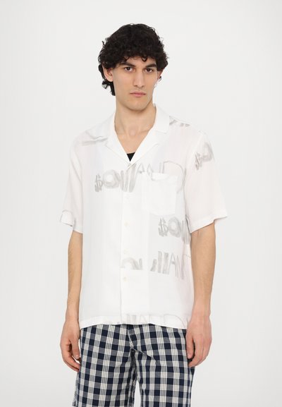 White short-sleeve shirt with a pocket, featuring a light gray dollar sign pattern. Worn with navy and white checkered shorts.
