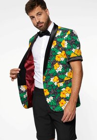 Květinový blazer s černými saténovými klopami, zdobený žlutými a bílými květinami na zelených listech, nošený přes bílou košili a černé šortky.