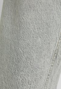 Tela de denim en gris claro con una superficie texturizada, que presenta un diseño clásico de cinco bolsillos y detalles de costura en contraste a lo largo de las costuras.