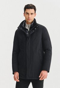 Czarna ocieplana kurtka z wysokim kołnierzem, z zatrzaskami i zapinaną na zamek wewnętrzną podszewką. Posiada elegancki wygląd i boczne kieszenie.