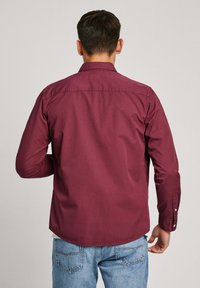 Bordeaux lange mouw shirt met een kraag met knopen, getailleerde pasvorm en een afgeronde zoom. De stof heeft een gladde textuur. Voorzien van knoopmanchetten.