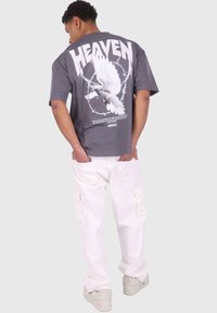 Un tricou grafic gri, cu textul "HEAVEN" și un design cu o porumbel alb, combinat cu pantaloni cargo albi și adidași.