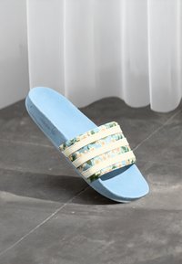 Sandală albastră tip slide cu trei benzi albe cu dungi florale, având o talpă moale din spumă și un finisaj neted texturat.