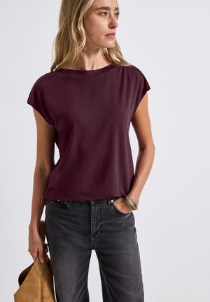 Burgundy short-sleeve top with a relaxed fit, smooth texture, and crew neckline, paired with dark gray jeans and a beige handbag.