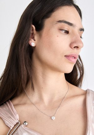 Zilveren hartvormige oorbellen en een ketting met een delicate ketting, met een heldere edelsteenaccent op de hanger. Glad, gepolijst oppervlak.