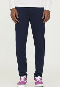Navyblauwe broek met een slim fit, gemaakt van een gladde stof, voorzien van standaardzakken en gecombineerd met paarse sneakers.
