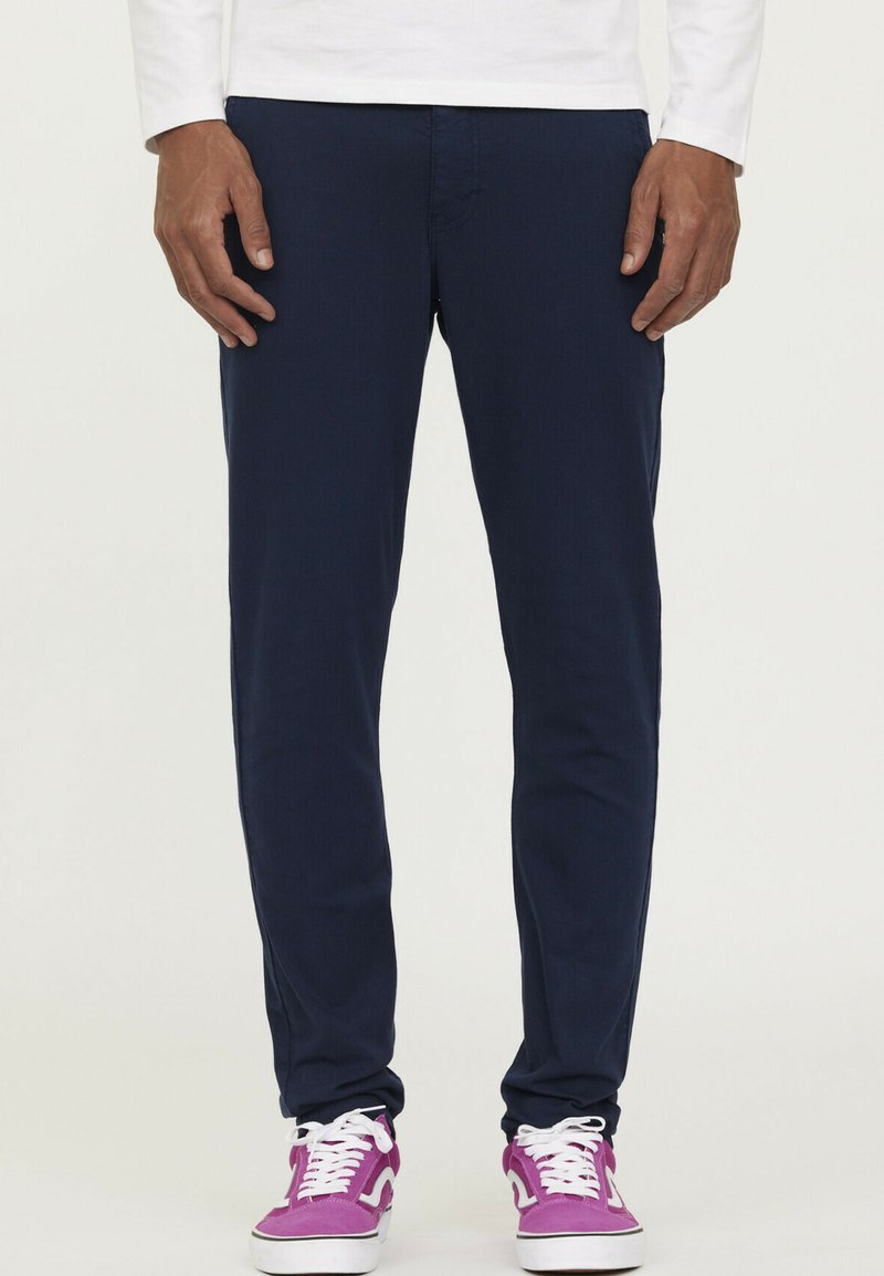 Navyblauwe broek met een slim fit, gemaakt van een gladde stof, voorzien van standaardzakken en gecombineerd met paarse sneakers.