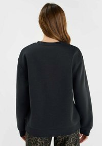 Svart sweatshirt med avslappnad passform, ribbad rund halsringning och långa ärmar, med en slät textur och rakt nederkant.