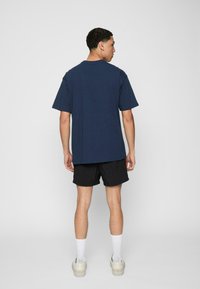 Marineblå oversized t-shirt med korte ærmer, parret med sorte shorts. Skoene er hvide med en klar sål, og sokkerne er hvide.