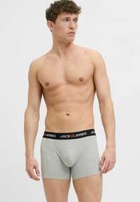 Pilkos spalvos bokso šortai su juodu juosmeniu, ant kurio baltais simboliais užrašyta prekės ženklas "JACK & JONES". Lygus audinio paviršius.