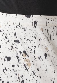 White fabric with a black and beige splatter pattern, smooth texture, featuring a black waistband. Design has a contemporary artistic style.