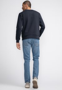 Marineblauwe sweatshirt met ronde halslijn en geribbelde manchetten, gecombineerd met lichtblauwe jeans en lichtgekleurde sneakers. Achteraanzicht.