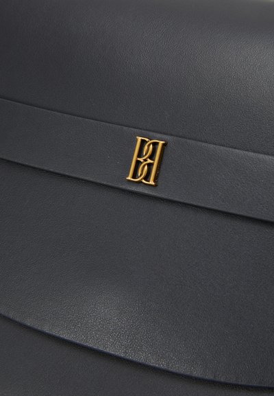 Un sac à main en cuir noir qui présente une texture lisse, un design courbé et un accent en logo doré. Simple et élégant, sans quincaillerie visible.